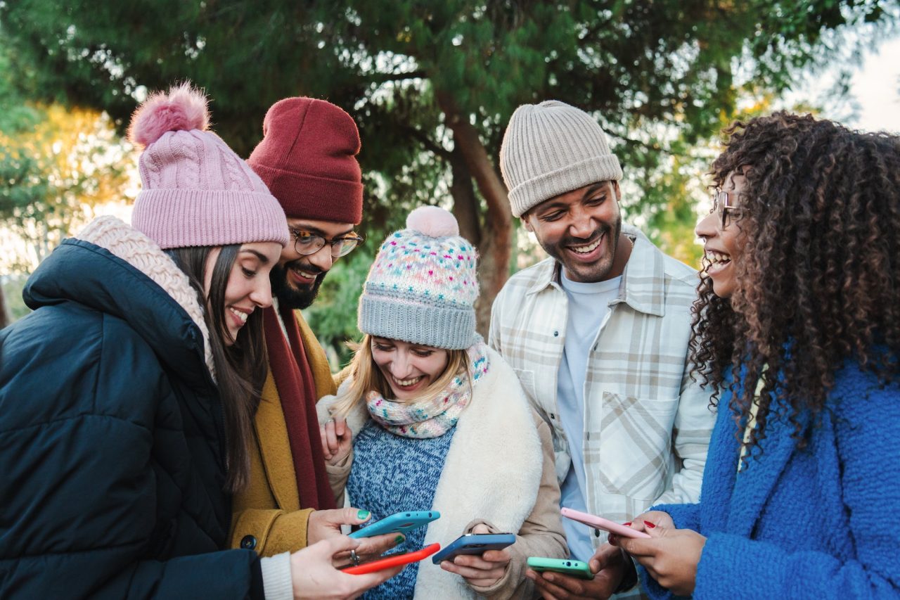 Group Of Multiracial Young Friends With Coats And Hats Smiling And Watching The Social Media With A.jpg